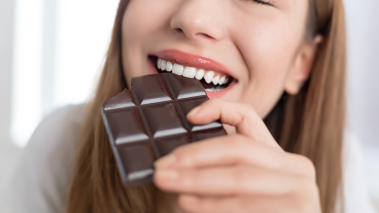 Une femme avec des dents dévitalisées qui mord à pleines dents une tablette de chocolat