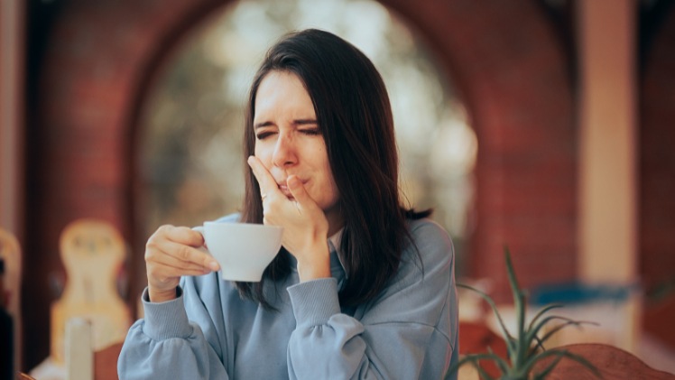 Une femme qui a les dents sensibles à une boisson chaude