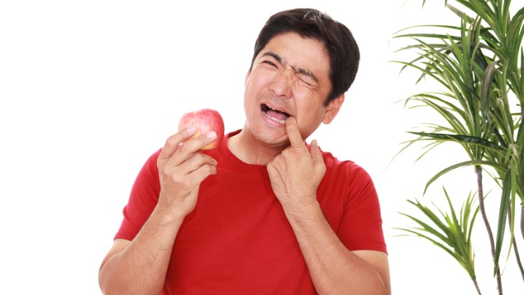 Un homme avec une sensibilité dentaire à l'acide d'une pomme